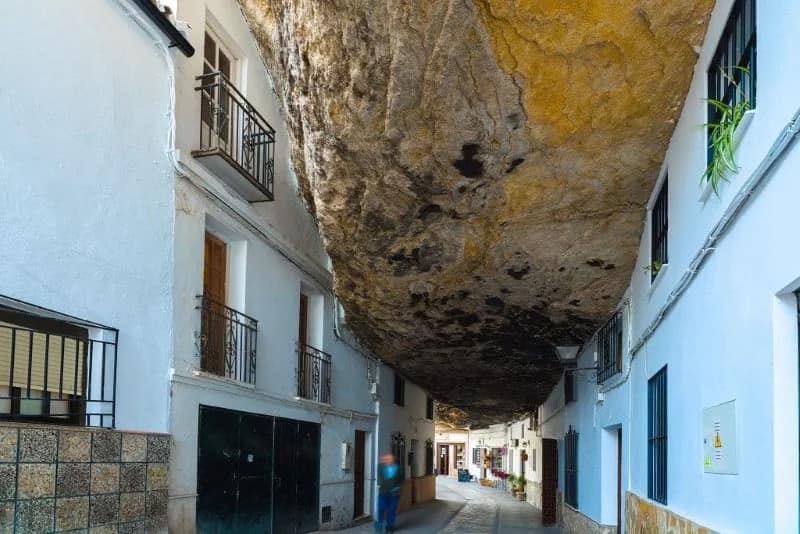 Wąska ulica w Setenil de las Bodegas z białymi domami po obu stronach i ogromnym skalnym nawisem zamiast nieba