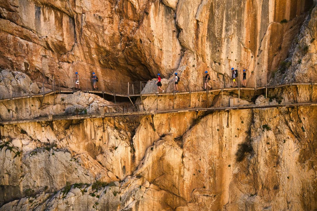 Grupa turystów w niebieskich kaskach idąca kładkami Caminito del Rey wzdłuż pionowej ściany