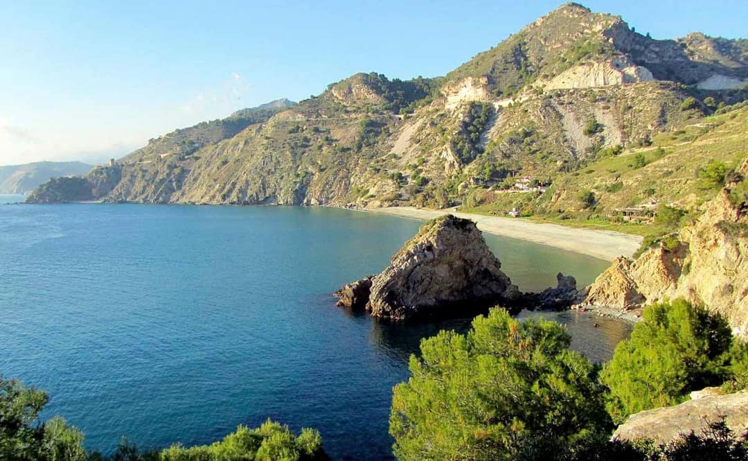 Klify Maro-Cerro Gordo koło Nerja: turkusowa zatoka, skała w wodzie, piaszczysta plaża i góry schodzące do morza